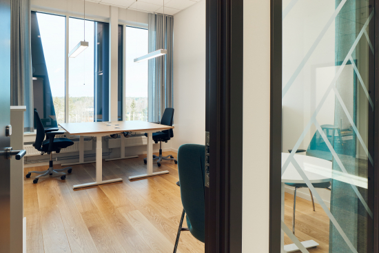 Kontorsrum för två personer med skrivbord, kontorsstolar, besöksstolar och bord.